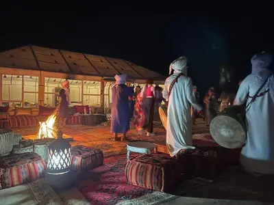 a group of people standing around a fire in a tent at Merzouga Majestic Camp in Merzouga