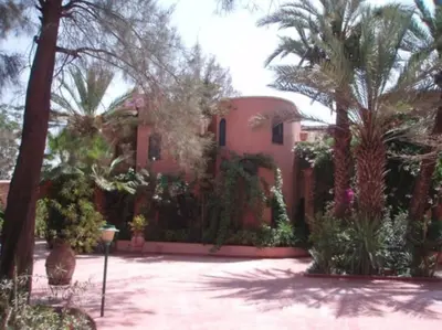 a large pink house with palm trees and plants at Villa Yasmina in Douar Blidene