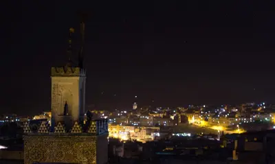 a lit up city at night with a clock tower at Riad Sanaa Rose in Fès