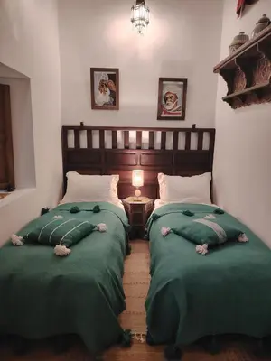a bedroom with two beds with green blankets and a table at La Maison des Amis in Fès