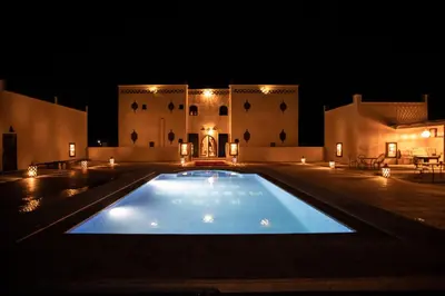 a large swimming pool in front of a building at night at Traditional Riad Merzouga Dunes in Merzouga
