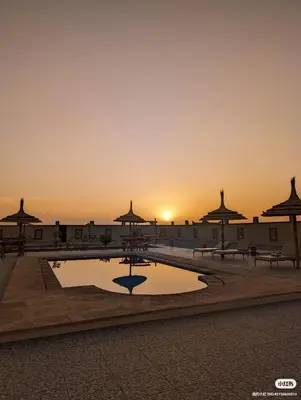 a pool in a courtyard with a sunset in the background at Traditional Riad Merzouga Dunes in Merzouga