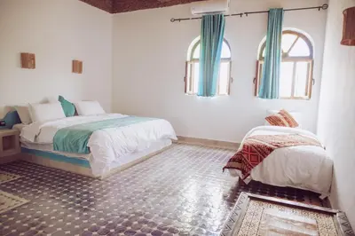 a bedroom with two beds and two windows at Traditional Riad Merzouga Dunes in Merzouga
