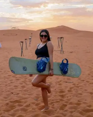 a woman standing in the desert holding a surfboard at Holiday Desert Camp in Merzouga