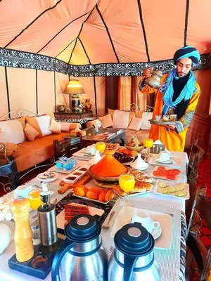 a man in a tent with a table full of food at Merzouga starlit desert camp in Hassilabied