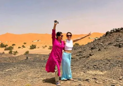 two women standing in the desert with their arms in the air at Merzouga Luxury Dunes Camp in Merzouga