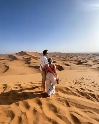 a man and woman walking through the desert at Diament Luxury Camp-Sahara Desert Experience in Merzouga in Merzouga