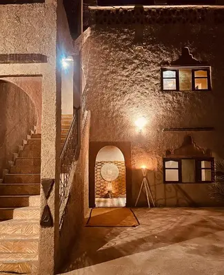 a stone building with a staircase and a light at Hotel Camping Les Roses Des Dunes & Piscine in Merzouga