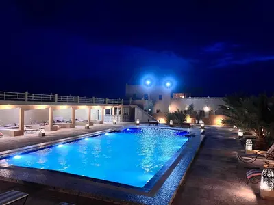 a large swimming pool at night with lights at Hotel Camping Les Roses Des Dunes & Piscine in Merzouga