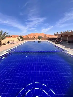 a blue swimming pool in the middle of the desert at Hotel Camping Les Roses Des Dunes & Piscine in Merzouga