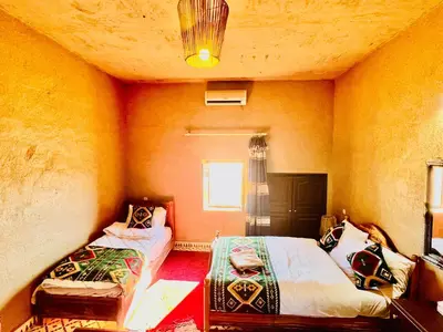 a bedroom with two beds in a room with orange walls at Hotel Camping Les Roses Des Dunes & Piscine in Merzouga