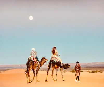 a group of three people riding camels in the desert at Hotel Camping Les Roses Des Dunes & Piscine in Merzouga