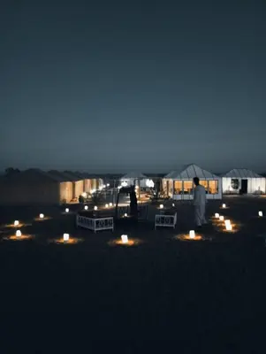 a man standing in front of a tent at night at lecherif luxury Camps in Merzouga