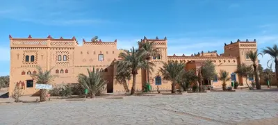 a large building with palm trees in front of it at Hotel le Touareg in Merzouga
