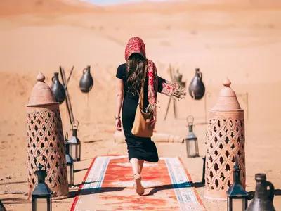 a woman walking on the sand in the desert at Merzouga Comfortable Camps in Merzouga