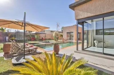 a home with a swimming pool and a patio with an umbrella at Villa Sakina, piscine Chauffée, ping-pong, cuisinière in Marrakech