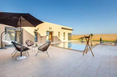 a patio with chairs and an umbrella and a pool at Villa Kassia , Jacuzzi, Hamman, jeux… in Marrakech