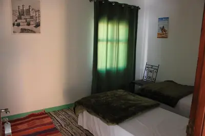 a bedroom with two beds and a window with green curtains at Kasbah lucas in Akhendachou nʼAït Ouffi