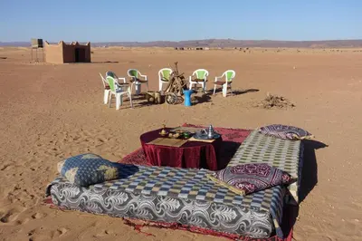 a bed and chairs in the sand in the desert at Sahara Berber Camp - Mhamid Discovery Camp in Mhamid El Ghizlane