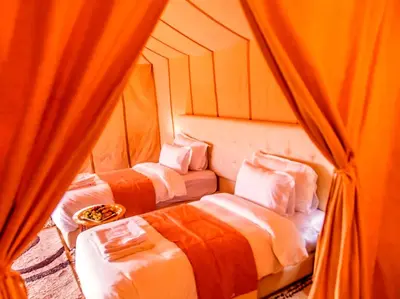 three beds in a room with orange curtains at Sahara Deluxe Camp in Merzouga