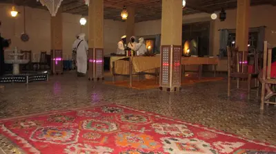 a room with a persian rug on the floor and people in a table at SANDSTAR PALACE in Merzouga