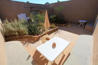 a patio with a white table and chairs and a table and a umbrella at Auberge Chez Julia in Merzouga