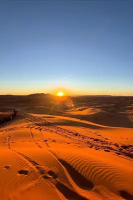 a sunset in the desert with tracks in the sand at Sahara Magic luxury Camp in Merzouga