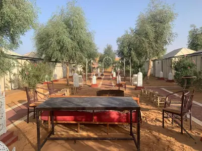 a park with chairs and a table and trees at Desert night Camp in Merzouga