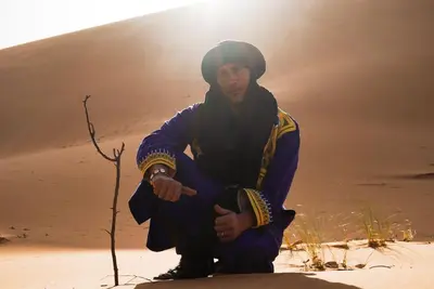 a man kneeling in the sand in the desert at Oasis Desert Camp Obira in Merzouga