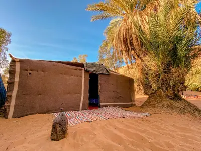 a small building in the sand with a palm tree at Oasis Desert Camp Obira in Merzouga
