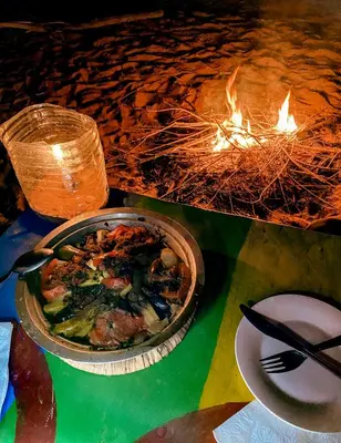 a table with a bowl of food next to a fire at Oasis Desert Camp Obira in Merzouga