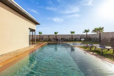 a swimming pool next to a building with palm trees at Villa Lella, piscine Chauffée, cuisinière in Marrakech