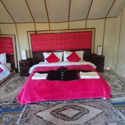 a bedroom with a large pink bed with red pillows at Luxury Sahara Camp in Merzouga