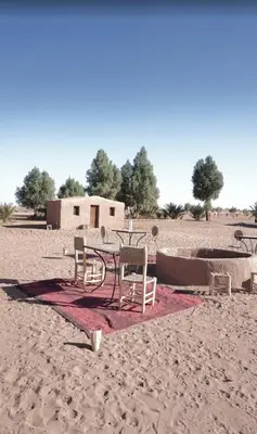 a table and chairs on the sand in the desert at Camp Bivouac Hassi Smara in Tâlhâ