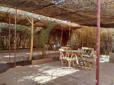 a patio with a table and chairs under a straw roof at Auberge chez hammadi in Zagora