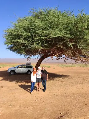 three people standing under a tree in front of a car at Auberge chez hammadi in Zagora