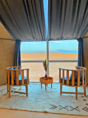 two chairs and a table in a room with the beach at Sky View Camp in Merzouga