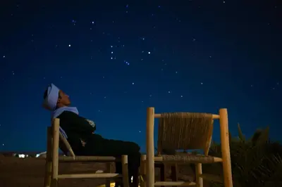 a man sitting in two chairs under the stars at Sky View Camp in Merzouga