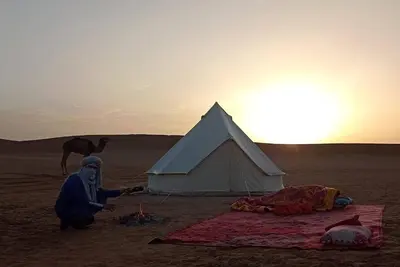 a man kneeling next to a tent in the desert at AUBERGE SAHARA IRIKI & Désert Tours in Foum Zguid