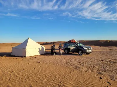 two people and a tent and a jeep in the desert at AUBERGE SAHARA IRIKI & Désert Tours in Foum Zguid