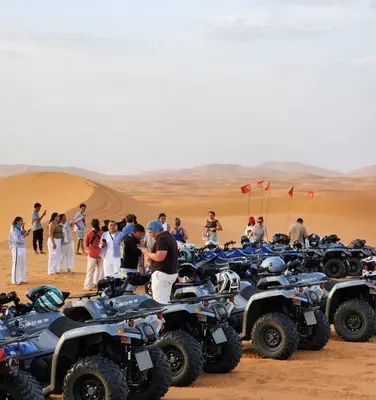 a group of people standing around a group of atvs in the desert at Sunshine luxury desert camp in Merzouga