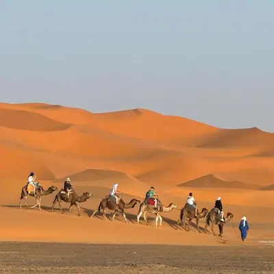 a group of people riding horses in the desert at Hotel Cafe Du Sud in Merzouga