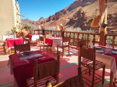 a restaurant with tables and chairs with mountains in the background at Hotel Atlas Gorge Dades in Boumalne