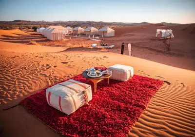 a desert with two beds and a table in the desert at Titanic Merzouga Camp in Merzouga