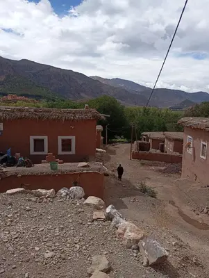 a person walking down a dirt road next to houses at Gite Timit la maison Imazghn in Azilal