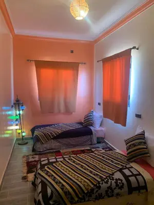 a bedroom with two beds and a window with orange curtains at Appartement Hassilabiad-Erg Chebbi in Hassilabied