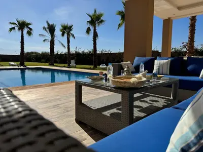 a patio with a table and a pool with palm trees at Bienvenu chez VillAtlas in Marrakech