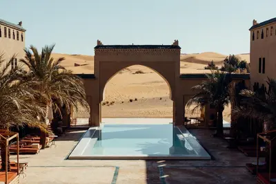 a pool in the middle of a desert with palm trees at Sahara pearl Hotel in Merzouga