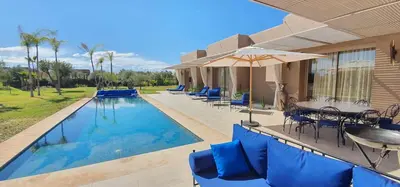 a swimming pool with blue chairs and an umbrella at Villa à 30 mn de Marrakech. in El Aouina