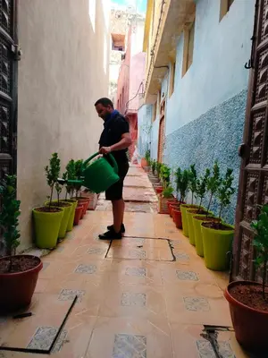a man standing in an alley holding a green bucket at Riad Andalousse in Meknès